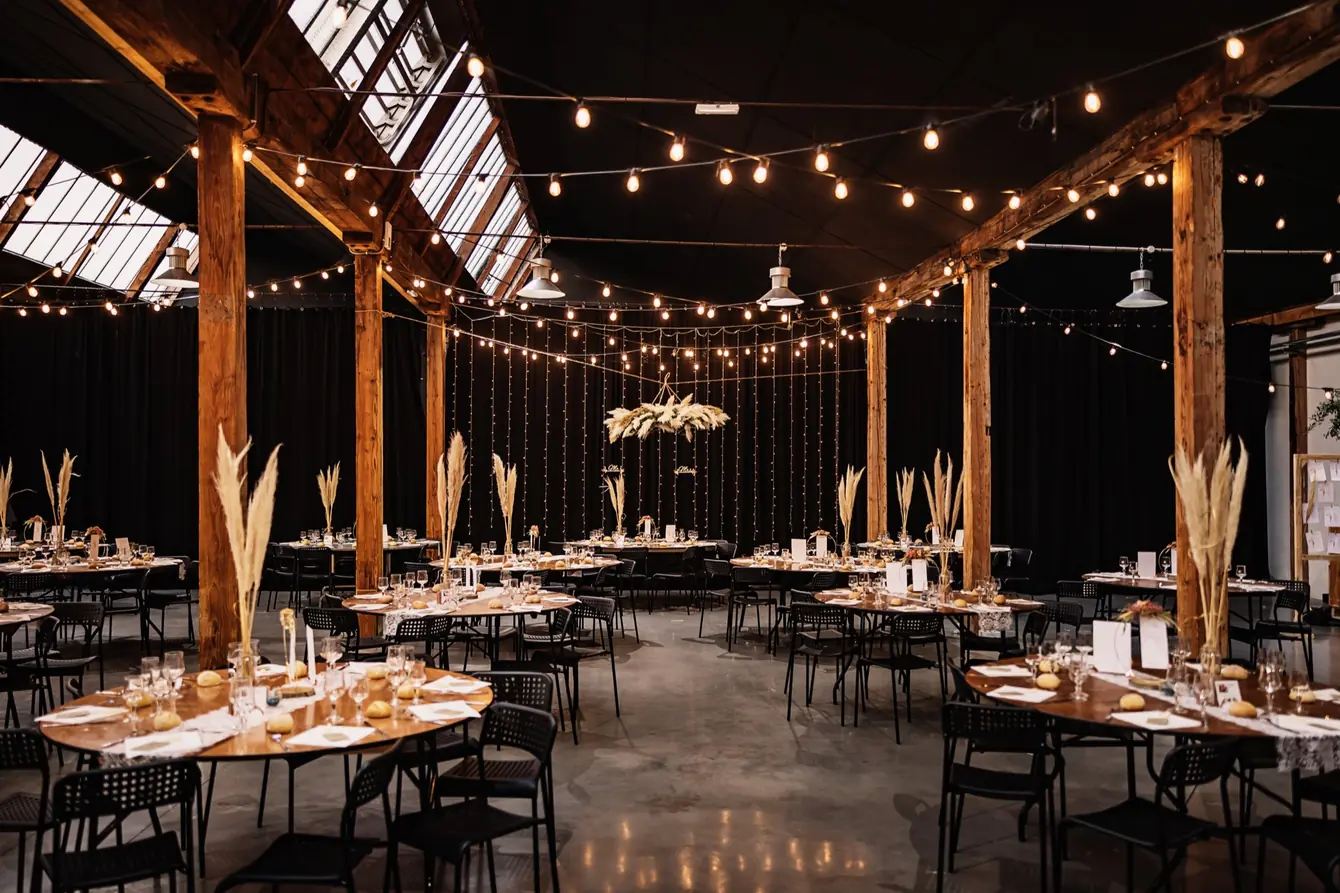 La grande salle du domaine : poutres en bois, guirlandes lumineuses, tables rondes et herbes de la pampa